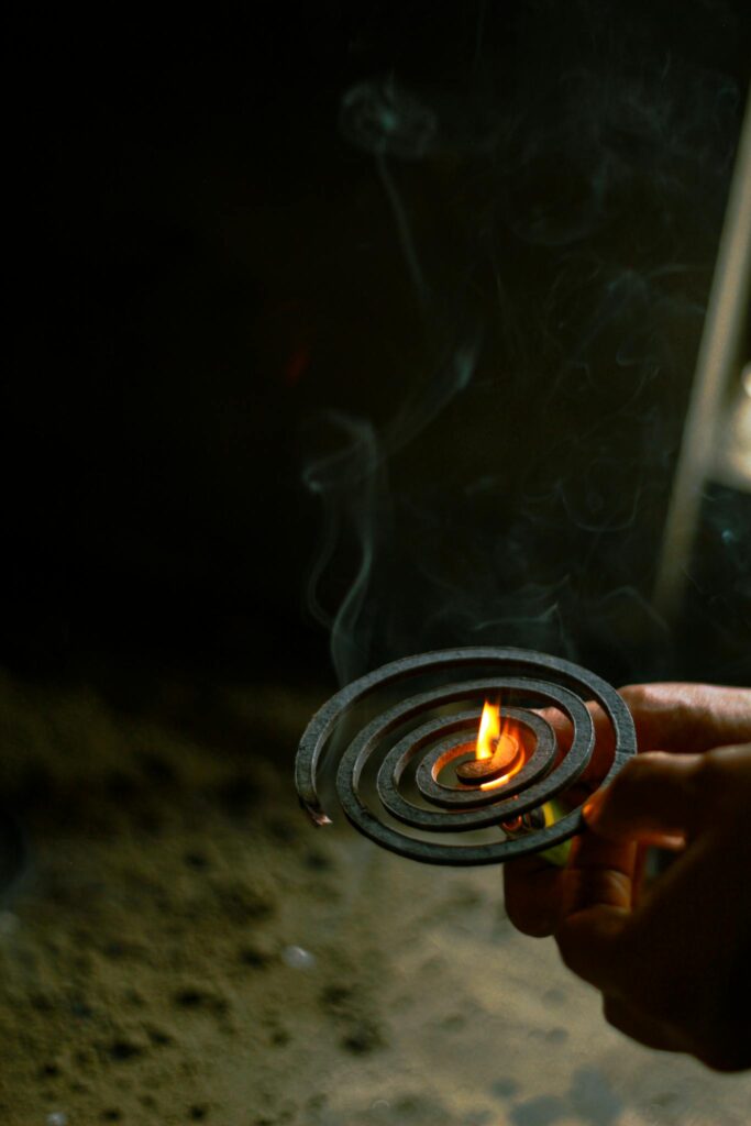 A hand igniting a mosquito coil, producing smoke in dim lighting, symbolizing protection.